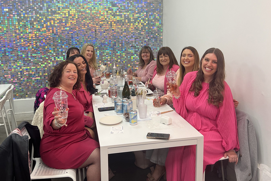 Hen party wearing hot pink raise their champagne glasses in front of glittery wall